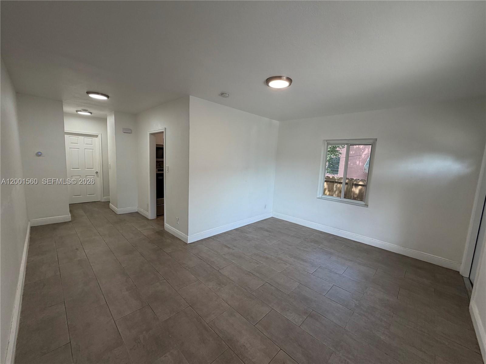 An empty room features white walls, gray tile flooring, two ceiling lights, and a window — 7712 NE 1st Ct, Miami FL 33138, MIAMI, FL