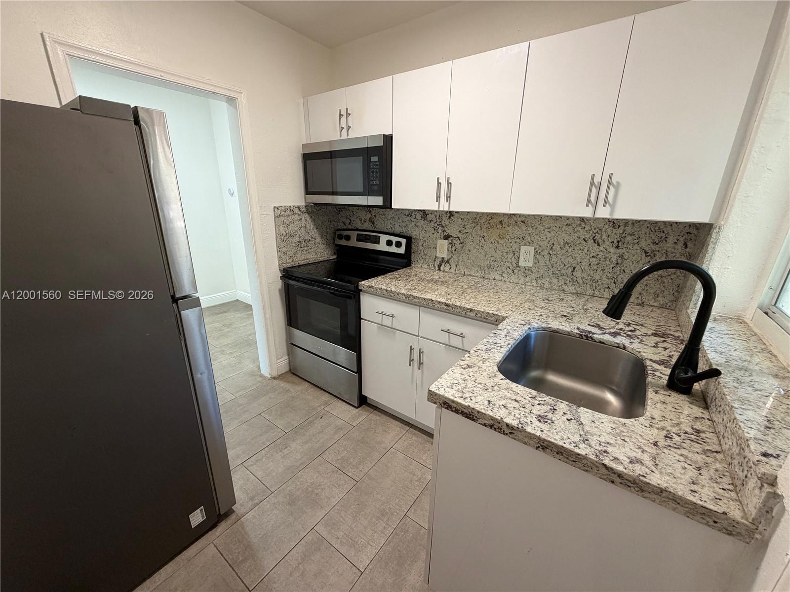 A kitchen features white cabinets, granite countertops, stainless steel appliances, and a black faucet — 7712 NE 1st Ct, Miami FL 33138, MIAMI, FL