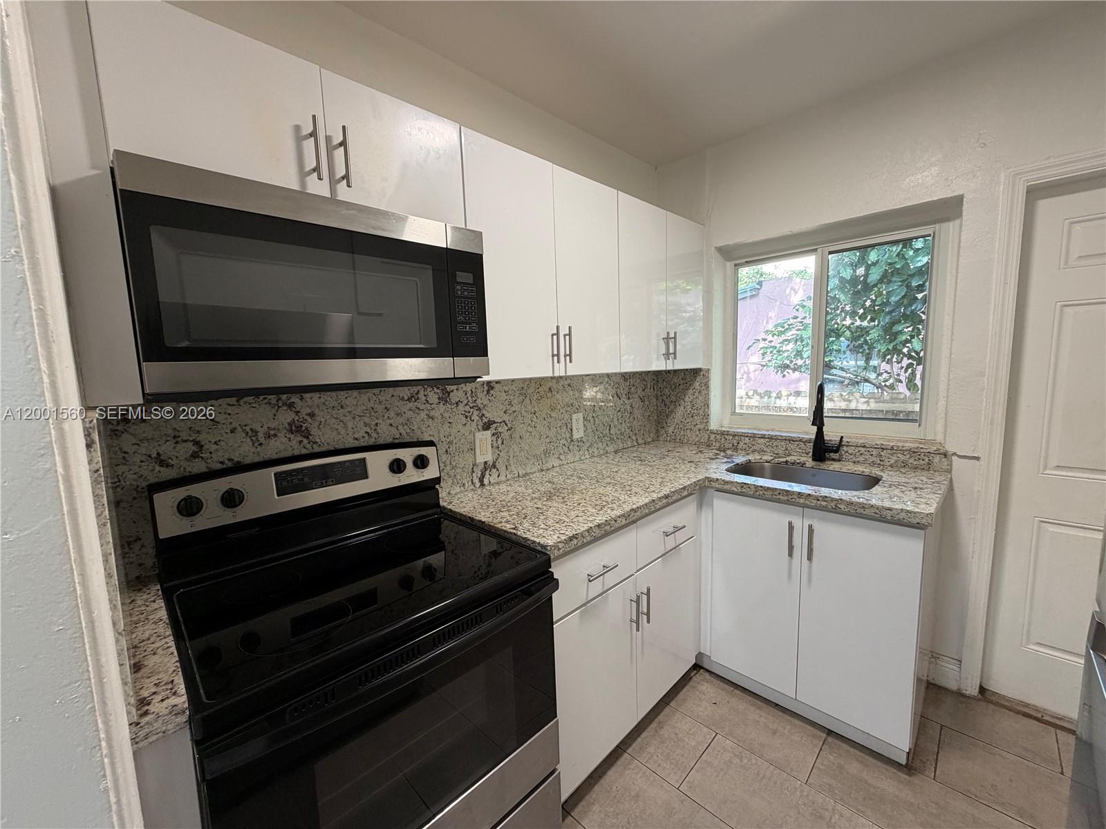 A kitchen features white cabinets, granite countertops, a black stove, and a stainless steel microwave — 7712 NE 1st Ct, Miami FL 33138, MIAMI, FL