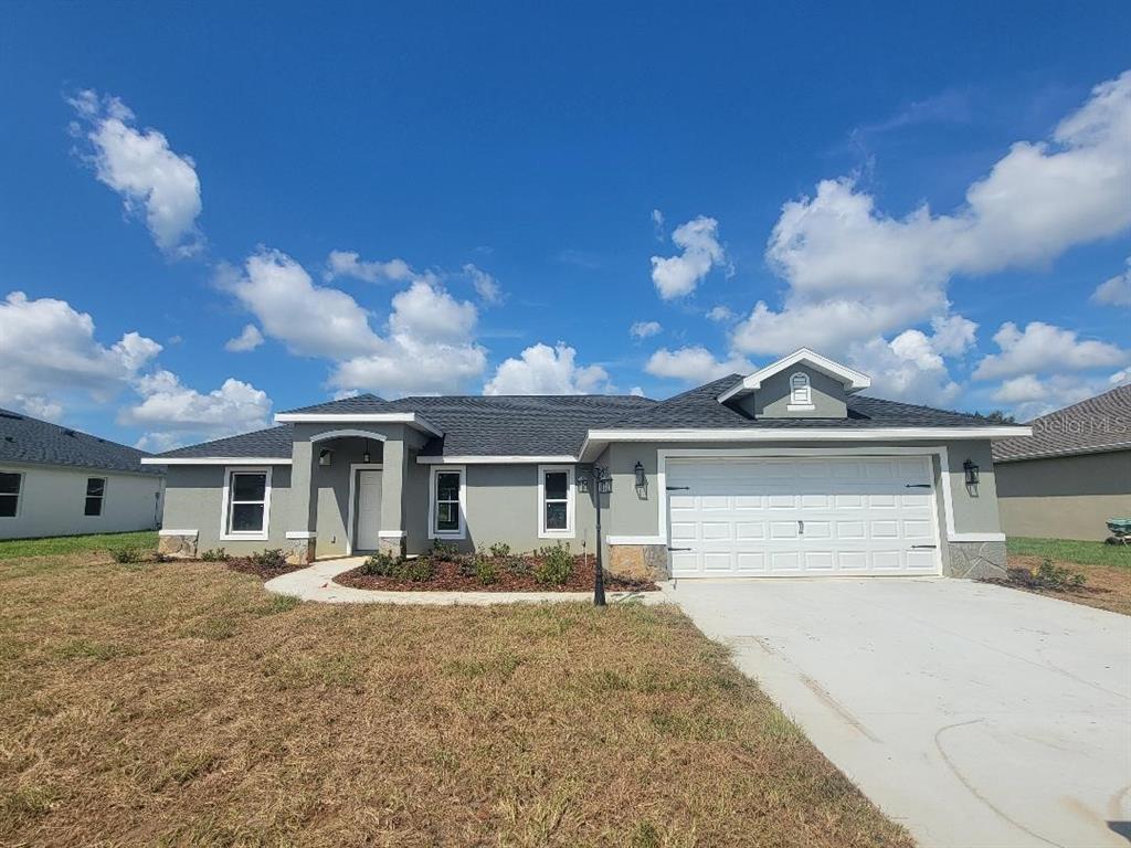 A single-story house with a gray stucco exterior, dark shingled roof, and a two-car garage — 5441 CHESTNUT RIDGE ROAD, DADE CITY, FL