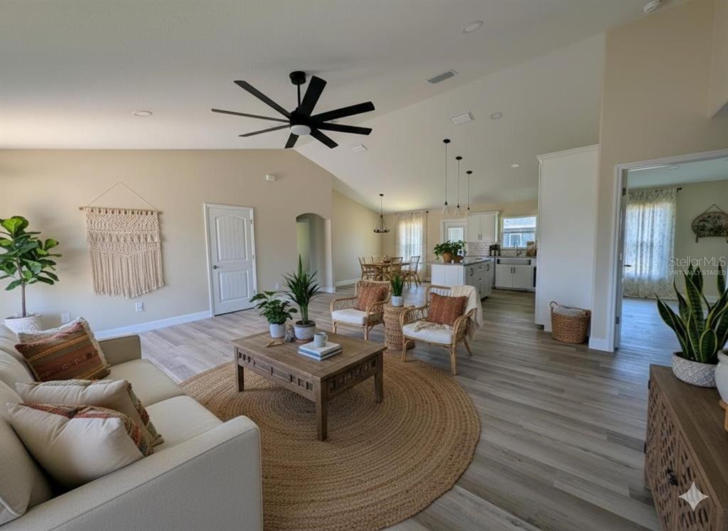 A living room with light wood flooring, a circular jute rug, and an open kitchen — 5441 CHESTNUT RIDGE ROAD, DADE CITY, FL