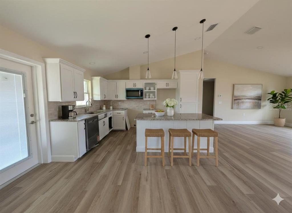 A kitchen with white cabinets, granite countertops, a center island with stools, and wood-look flooring — 5441 CHESTNUT RIDGE ROAD, DADE CITY, FL