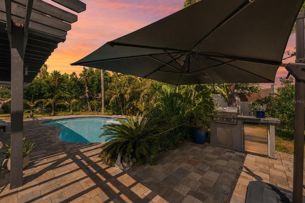 A backyard patio features a swimming pool, an outdoor kitchen, and a large cantilever umbrella — 14297 GENEVA DRIVE, LARGO, FL