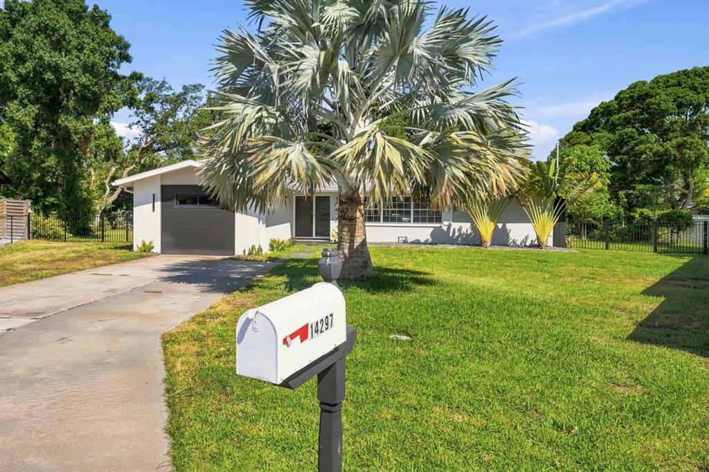 A white single-story house with a driveway and a large palm tree in the front yard — 14297 GENEVA DRIVE, LARGO, FL