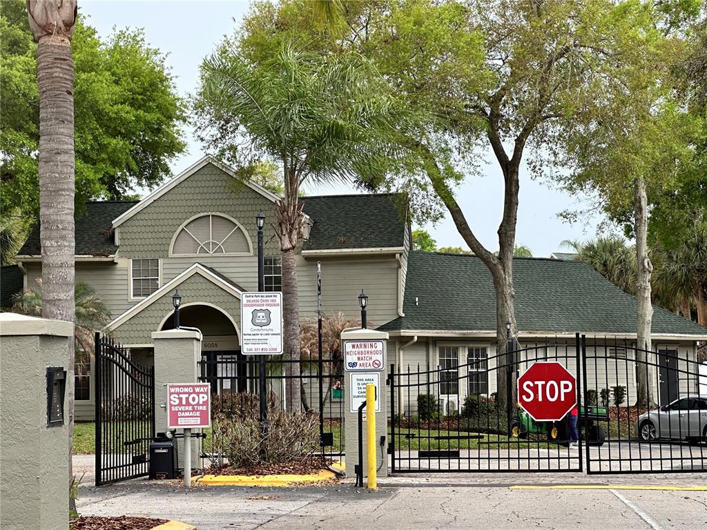 A gated entrance leads to a two-story building with green siding and a dark roof — 6004 WESTGATE DRIVE UNIT 301, ORLANDO, FL