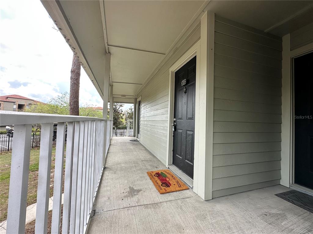 An outdoor apartment walkway features a black door, a holiday doormat, and a white railing — 6004 WESTGATE DRIVE UNIT 301, ORLANDO, FL