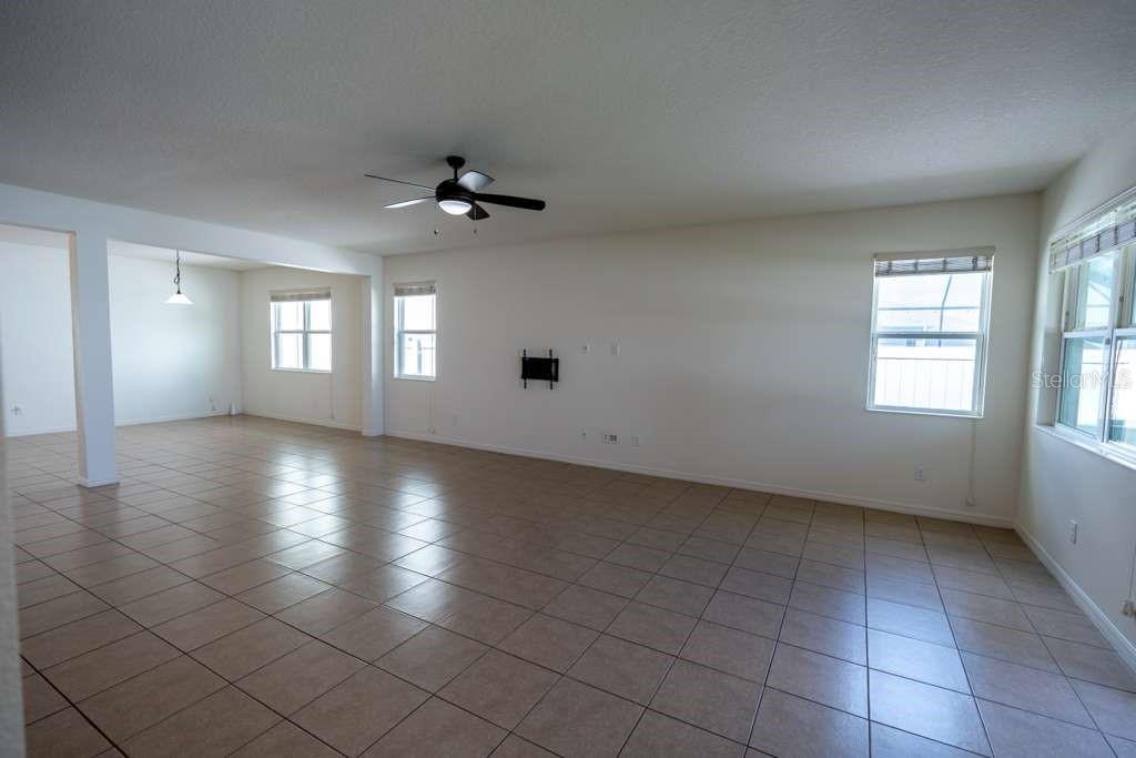 A spacious, open-concept living area features light-colored tile flooring, white walls, and a ceiling fan — 11517 PALMETTO SANDS COURT, TAMPA, FL