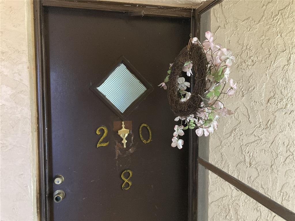 A brown front door features a diamond-shaped window, gold house numbers, and a floral wreath — 4164 HERON WAY UNIT 208, BRADENTON, FL