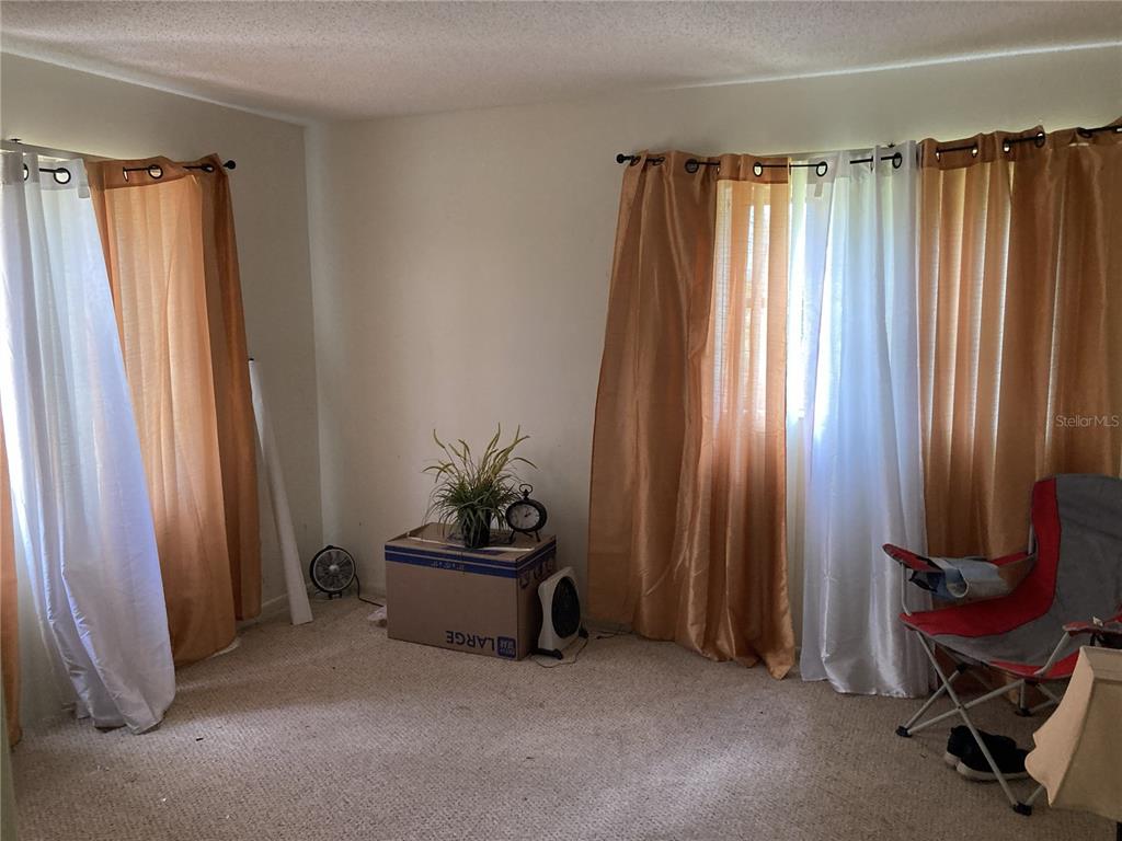 A room with beige carpet, white walls, two windows with layered curtains, and a cardboard box — 4164 HERON WAY UNIT 208, BRADENTON, FL