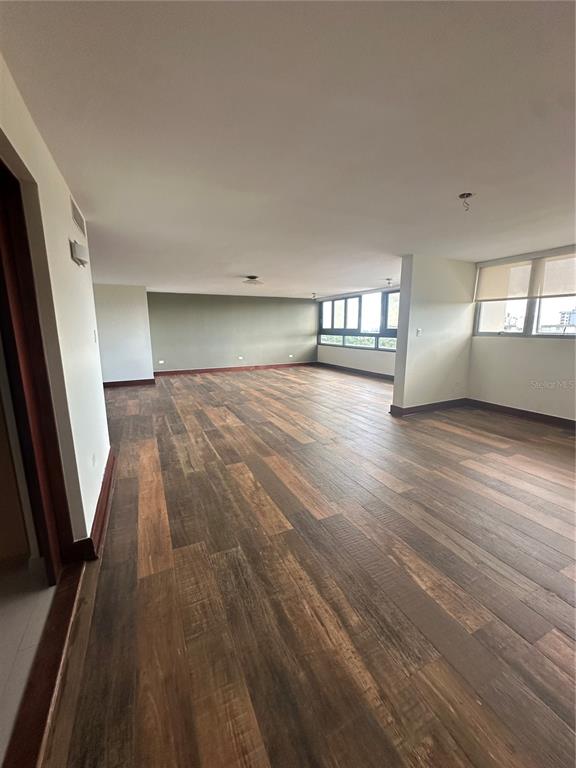 An empty room features wood-look tile flooring, white walls, and large windows — Caoba Street AVENIDA SAN PATRICIO UNIT PH1-PH2, GUAYNABO, PR