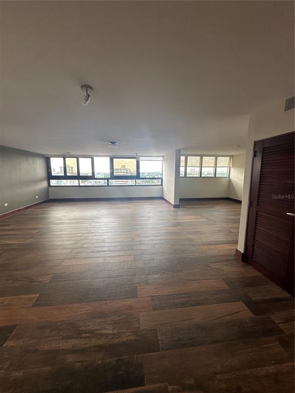 A spacious, empty room features wood-look tile flooring, white walls, and large windows with views — Caoba Street AVENIDA SAN PATRICIO UNIT PH1-PH2, GUAYNABO, PR
