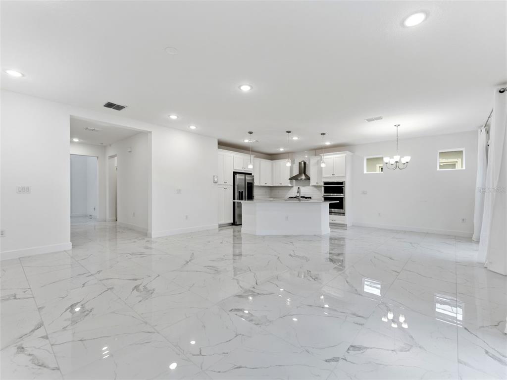 A bright, open-concept kitchen and living area featuring white cabinetry and polished marble-look tile flooring — 5232 WISHING ARCH DRIVE, APOLLO BEACH, FL