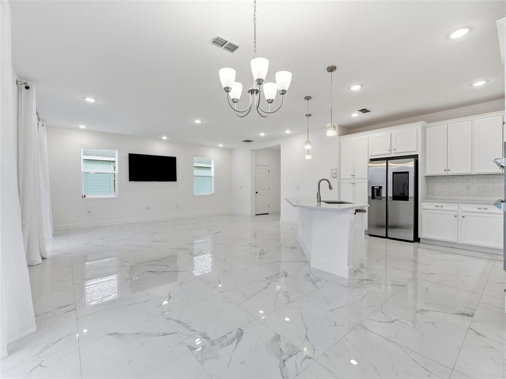 An open-concept kitchen and living area features white cabinetry, marble-look tile flooring, and a chandelier — 5232 WISHING ARCH DRIVE, APOLLO BEACH, FL