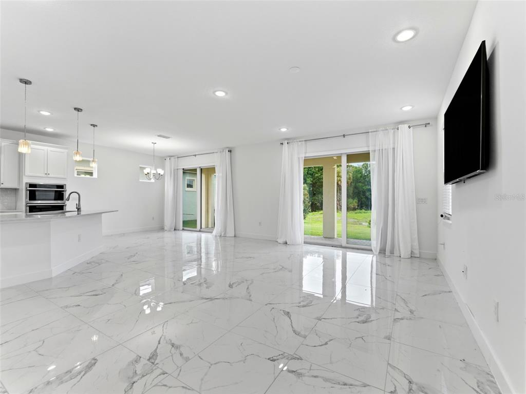 A bright, open-concept living area features white marble-look tile flooring and sliding glass patio doors — 5232 WISHING ARCH DRIVE, APOLLO BEACH, FL