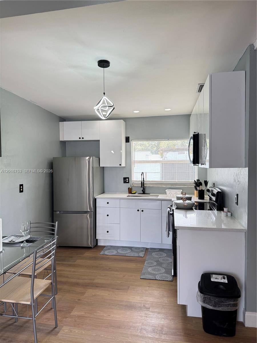 A kitchen features white cabinets, stainless steel appliances, and a modern geometric pendant light — 414 N 60th Way # 2, Hollywood FL 33024, HOLLYWOOD, FL