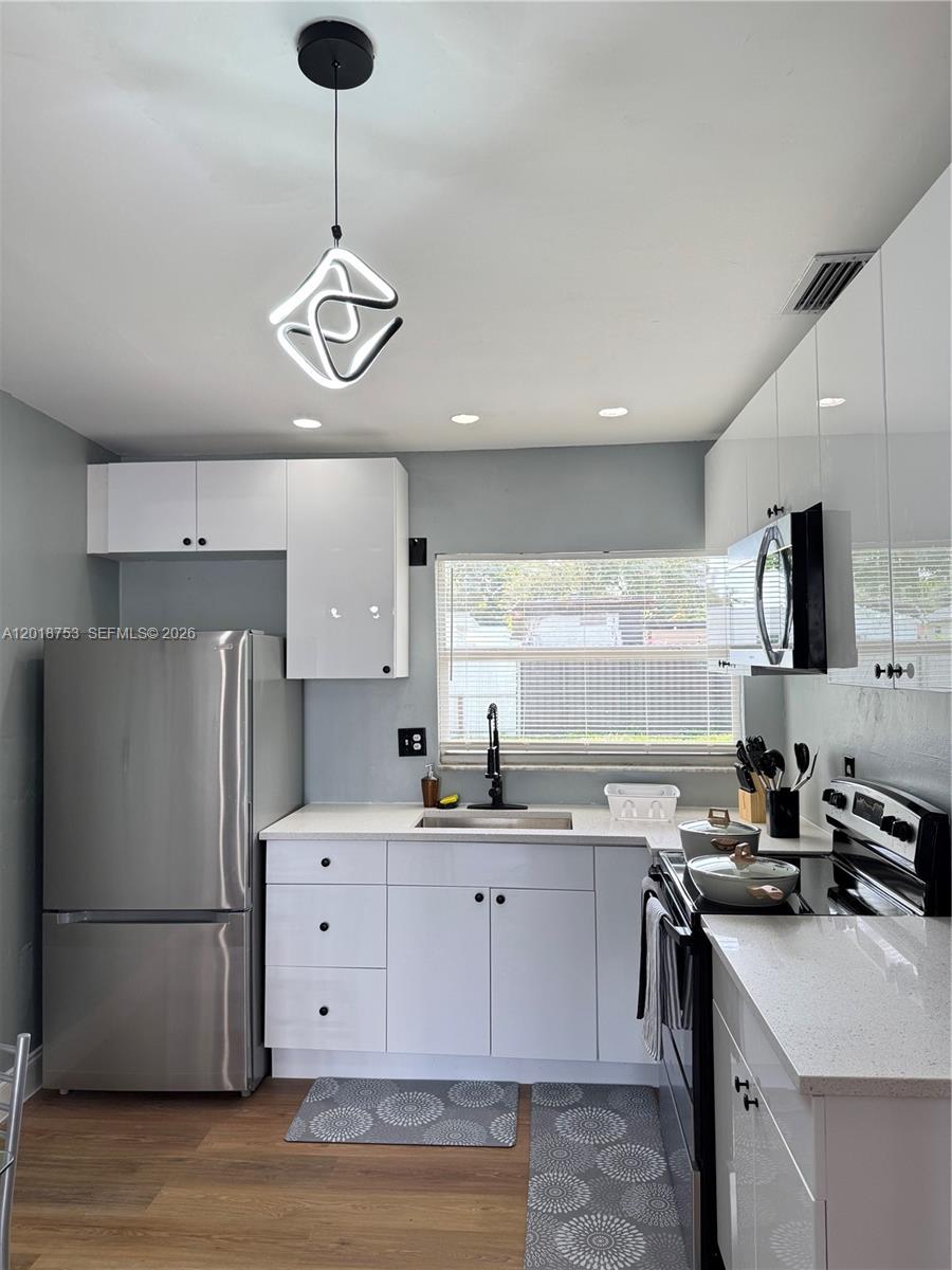 A modern kitchen features white cabinets, stainless steel appliances, and a unique geometric pendant light — 414 N 60th Way # 2, Hollywood FL 33024, HOLLYWOOD, FL