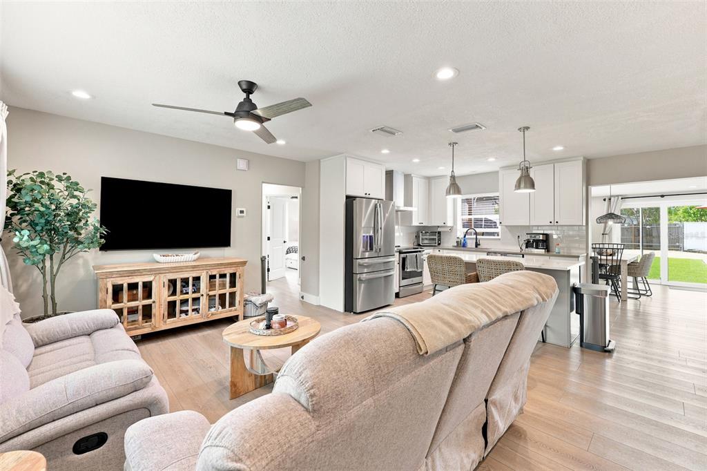 An open-concept living room and kitchen feature light wood flooring and white cabinetry — 716 75TH AVENUE N, ST PETERSBURG, FL