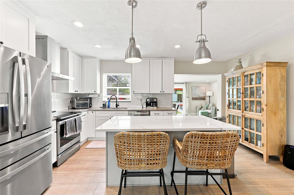 A modern kitchen features white cabinets, a marble-topped island with two wicker chairs, and stainless-steel appliances — 716 75TH AVENUE N, ST PETERSBURG, FL