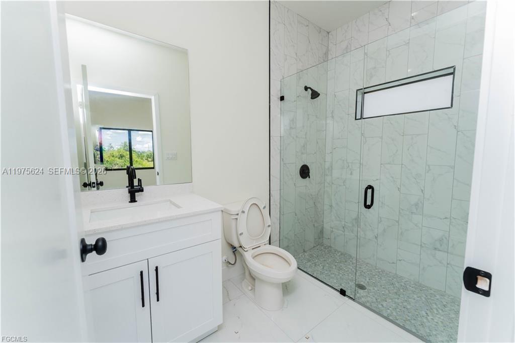 A modern bathroom features a white vanity, a toilet, and a glass-enclosed marble shower — 1171 countess ave, Lehigh Acres FL 33974, LEHIGH ACRES, FL