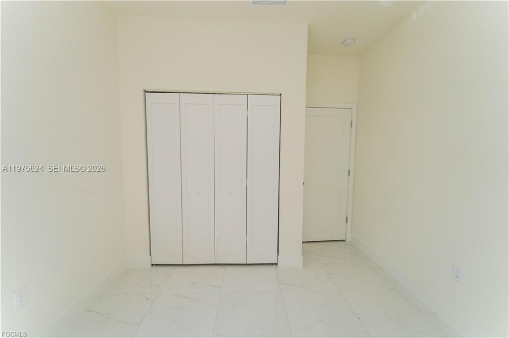 A room with white walls, white tile flooring, a four-panel closet, and a door — 1171 countess ave, Lehigh Acres FL 33974, LEHIGH ACRES, FL