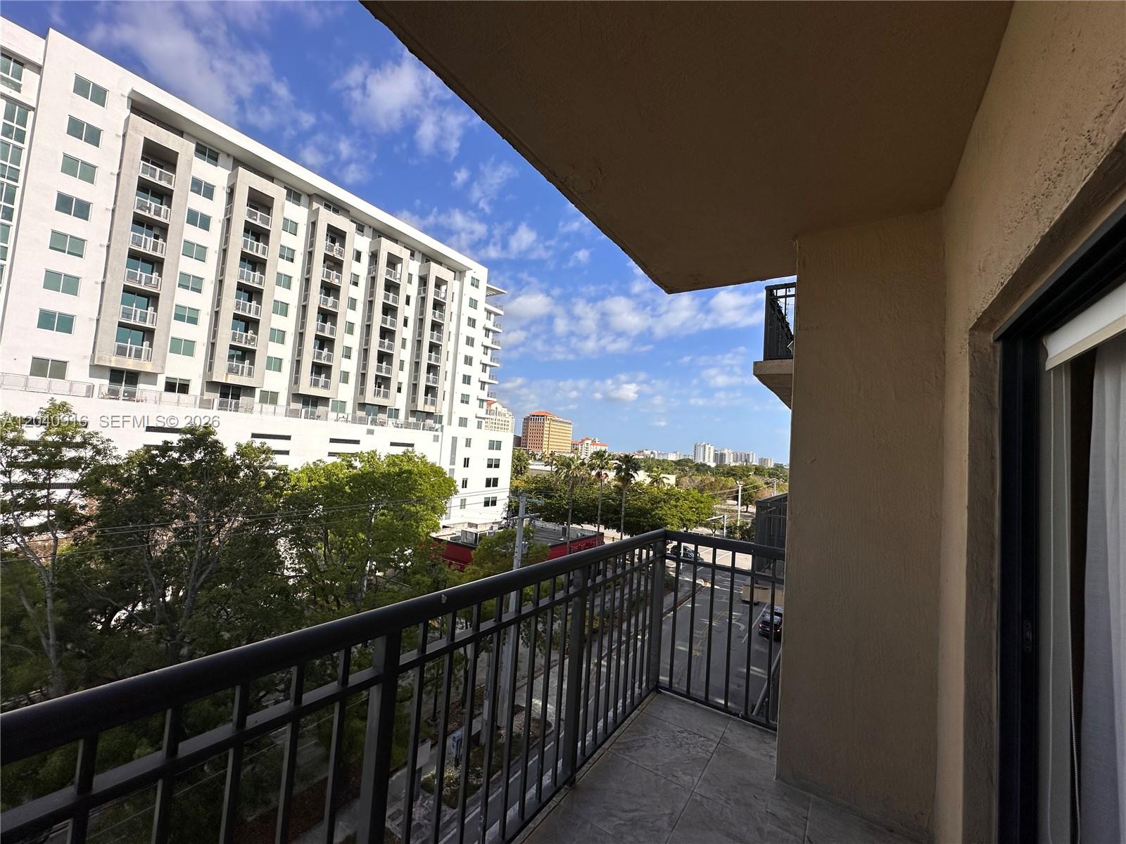 A balcony with a metal railing overlooks a street, trees, and a large apartment building — 3590 Coral Way # 611, Miami FL 33145, MIAMI, FL