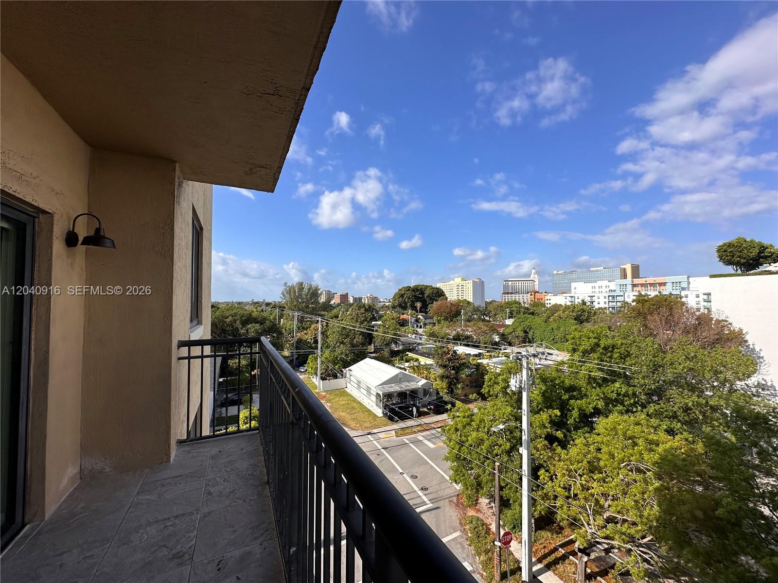 A balcony with a black metal railing overlooks a street, trees, and city buildings — 3590 Coral Way # 611, Miami FL 33145, MIAMI, FL