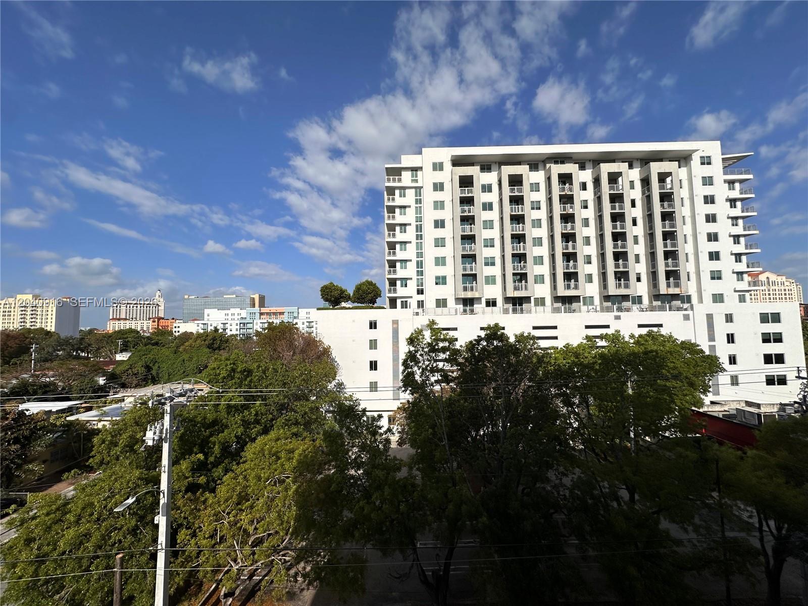 A large white apartment building stands against a blue sky with scattered clouds — 3590 Coral Way # 611, Miami FL 33145, MIAMI, FL