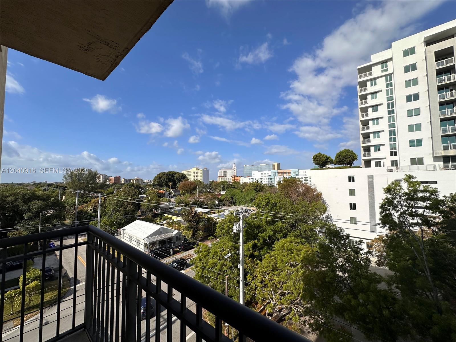 A balcony view overlooks a suburban street, lush trees, and nearby high-rise buildings — 3590 Coral Way # 611, Miami FL 33145, MIAMI, FL