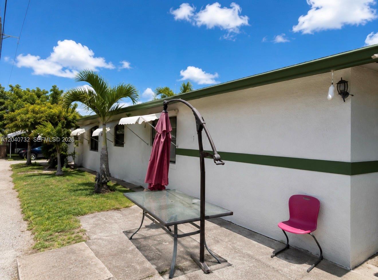 A glass-topped patio table with a closed umbrella and a pink chair sit outside — 141 SW 2nd St, Deerfield Beach FL 33441, DEERFIELD BEACH, FL