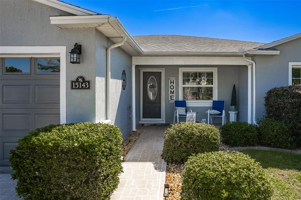 A gray house exterior features a front porch, a paved walkway, and manicured green bushes — 15143 SW 14TH AVENUE ROAD, OCALA, FL