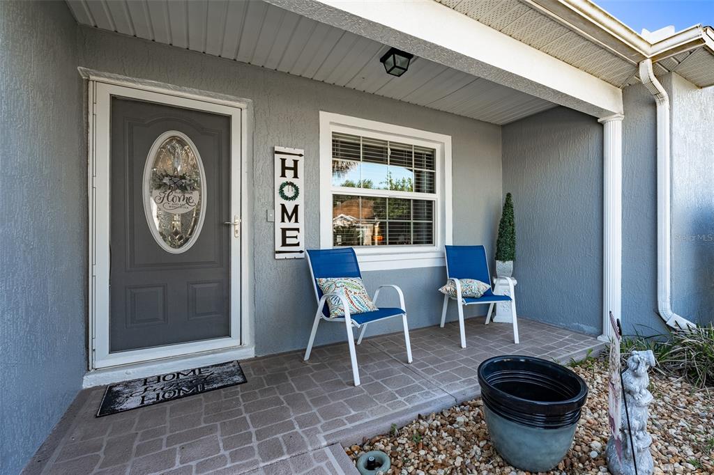 A covered front porch features a gray door, two blue chairs, and a tiled floor — 15143 SW 14TH AVENUE ROAD, OCALA, FL