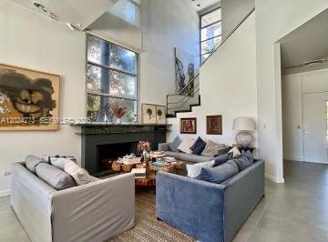 A living room features a fireplace, tall windows, a staircase, and two grey sofas — MA
