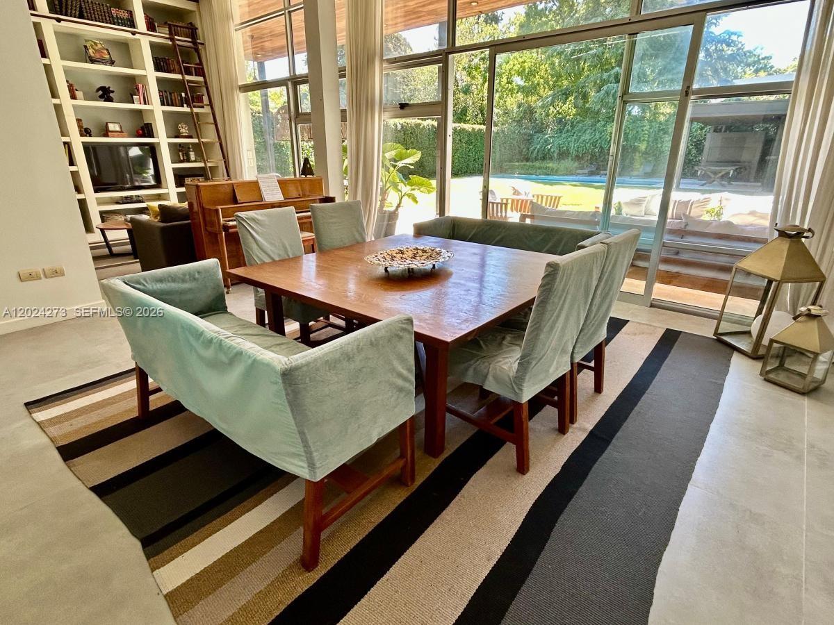 A dining room features a square wooden table, upholstered chairs, and floor-to-ceiling windows — MA