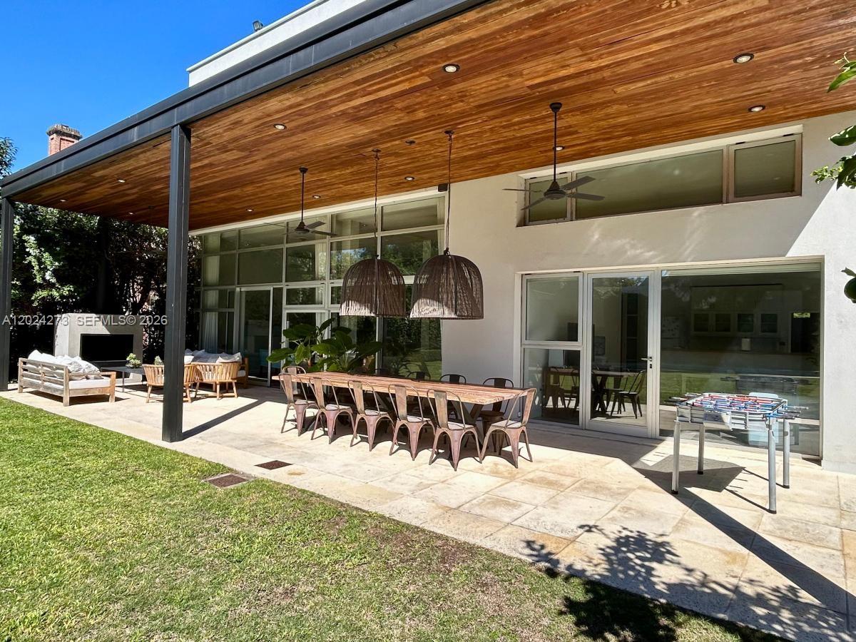 A covered outdoor patio features a long dining table, seating, and a foosball table — MA