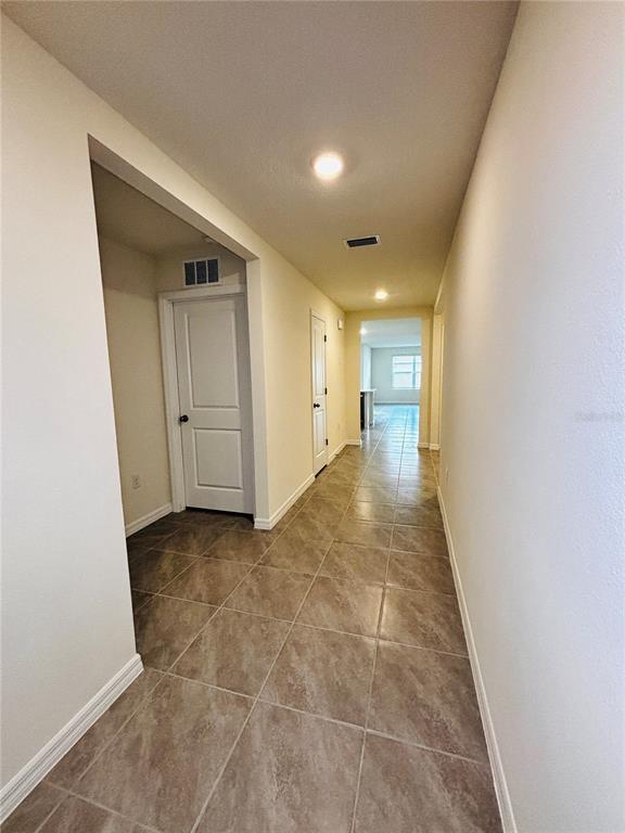 A hallway with tiled floors leads toward an open living area with a window — 1894 NW 247TH DRIVE, NEWBERRY, FL