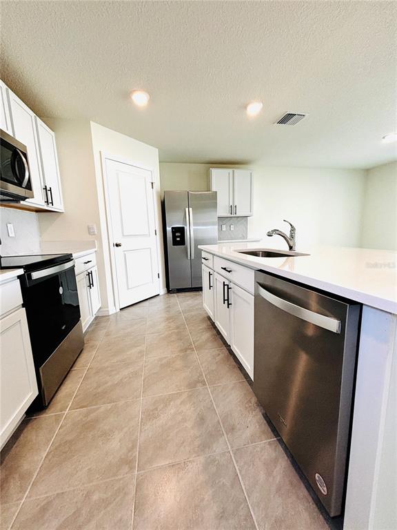 A kitchen features white cabinets, stainless steel appliances, and a large island with a sink — 1894 NW 247TH DRIVE, NEWBERRY, FL
