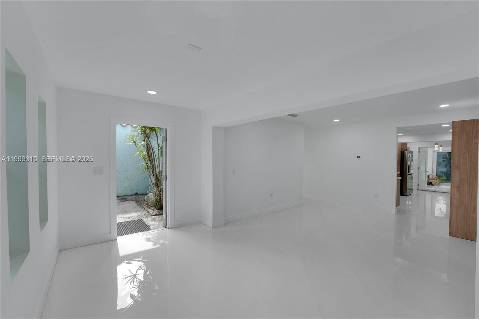 A bright, white-walled room features glossy tile floors, a doorway to a courtyard, and recessed lighting — FORT LAUDERDALE, FL