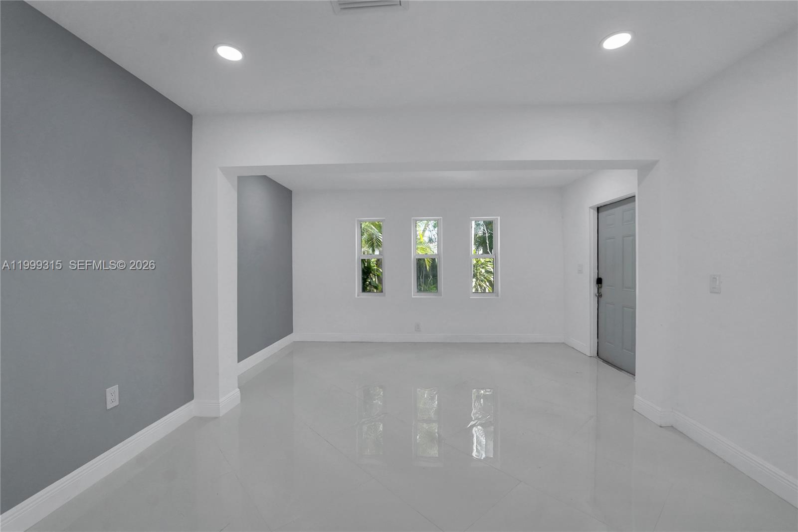 An empty room features white walls, a gray accent wall, tile flooring, and three windows — FORT LAUDERDALE, FL