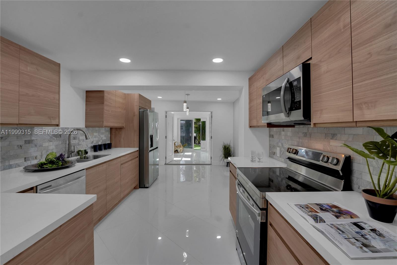 A modern kitchen features light wood cabinets, white countertops, stainless steel appliances, and tile flooring — FORT LAUDERDALE, FL