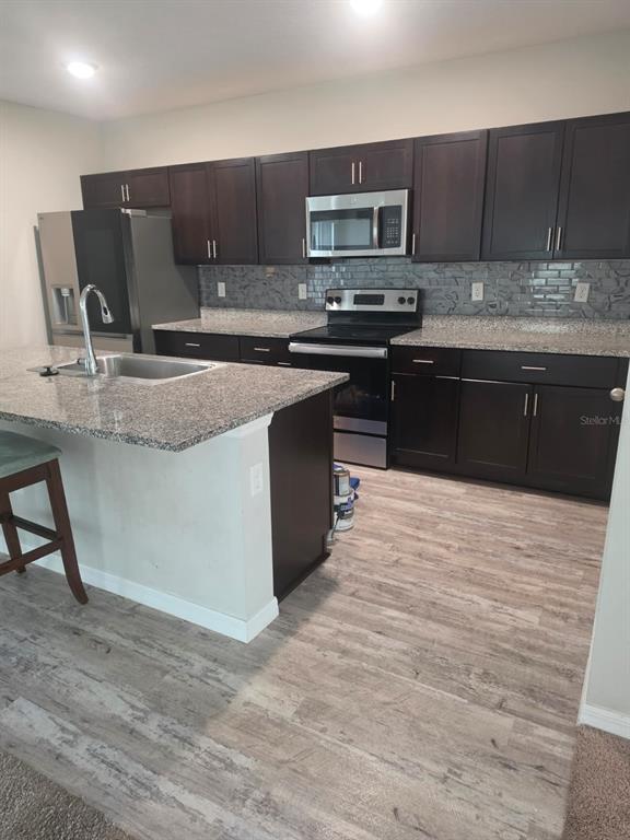 A kitchen features dark cabinets, granite countertops, a stainless steel refrigerator, and a breakfast bar — 13013 UPWARD PLACE, RIVERVIEW, FL