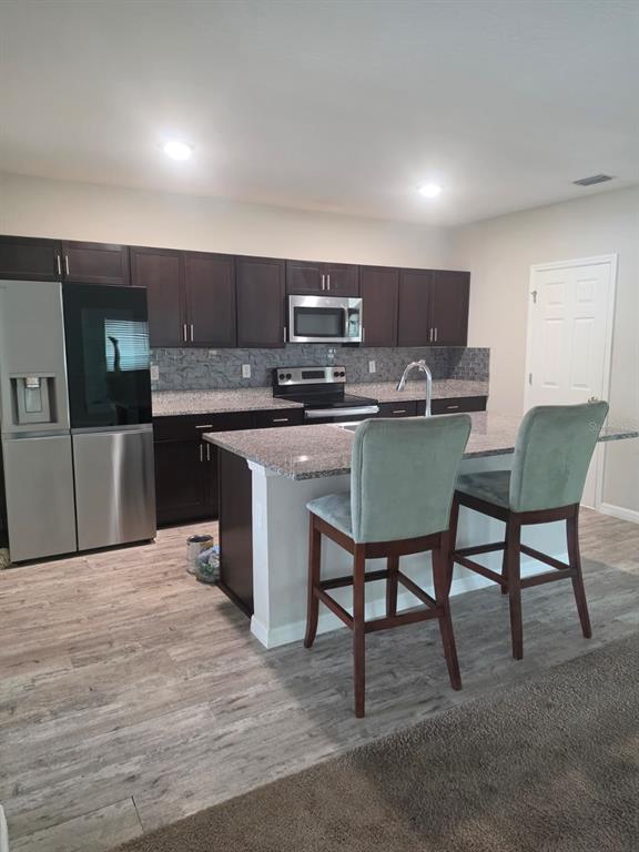 A kitchen features dark wood cabinets, granite countertops, stainless steel appliances, and wood-look flooring — 13013 UPWARD PLACE, RIVERVIEW, FL