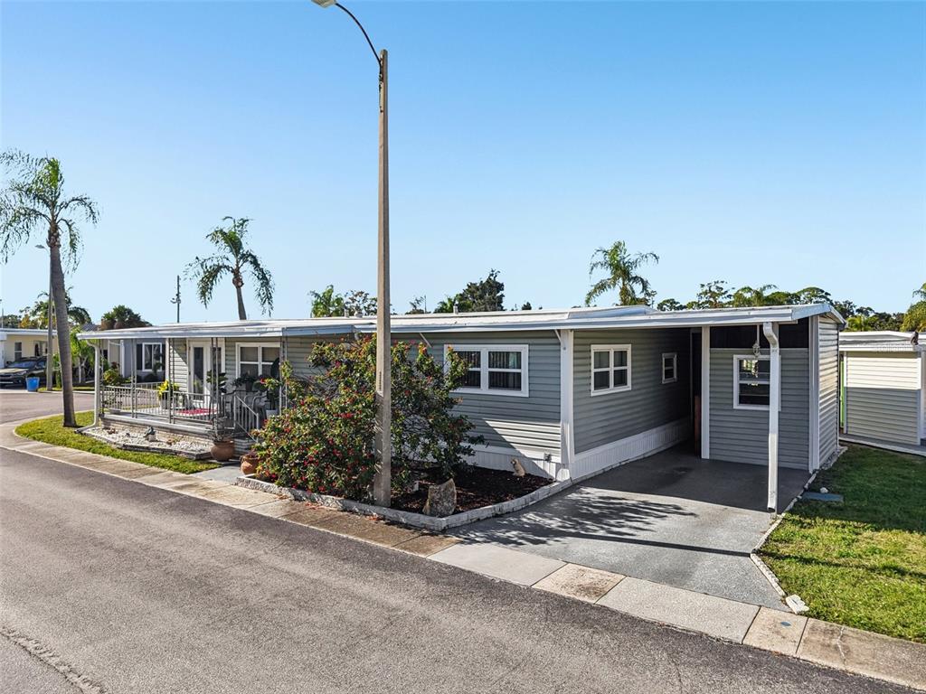 A single-story manufactured home with light gray siding, a front porch, and a carport — 82123 B STREET N UNIT 123, PINELLAS PARK, FL