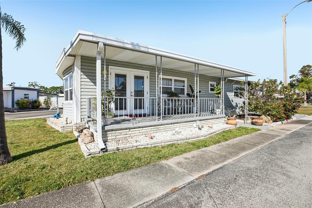 A light gray mobile home features a covered front porch with white railings and stairs — 82123 B STREET N UNIT 123, PINELLAS PARK, FL