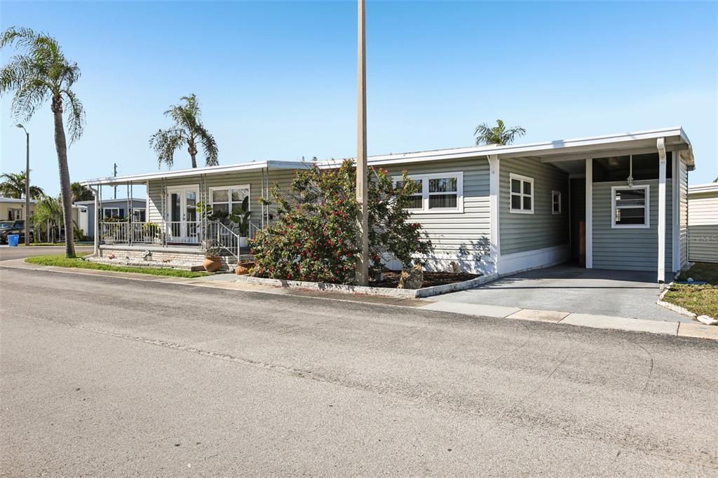 A light green manufactured home features a front porch, a carport, and a palm tree — 82123 B STREET N UNIT 123, PINELLAS PARK, FL