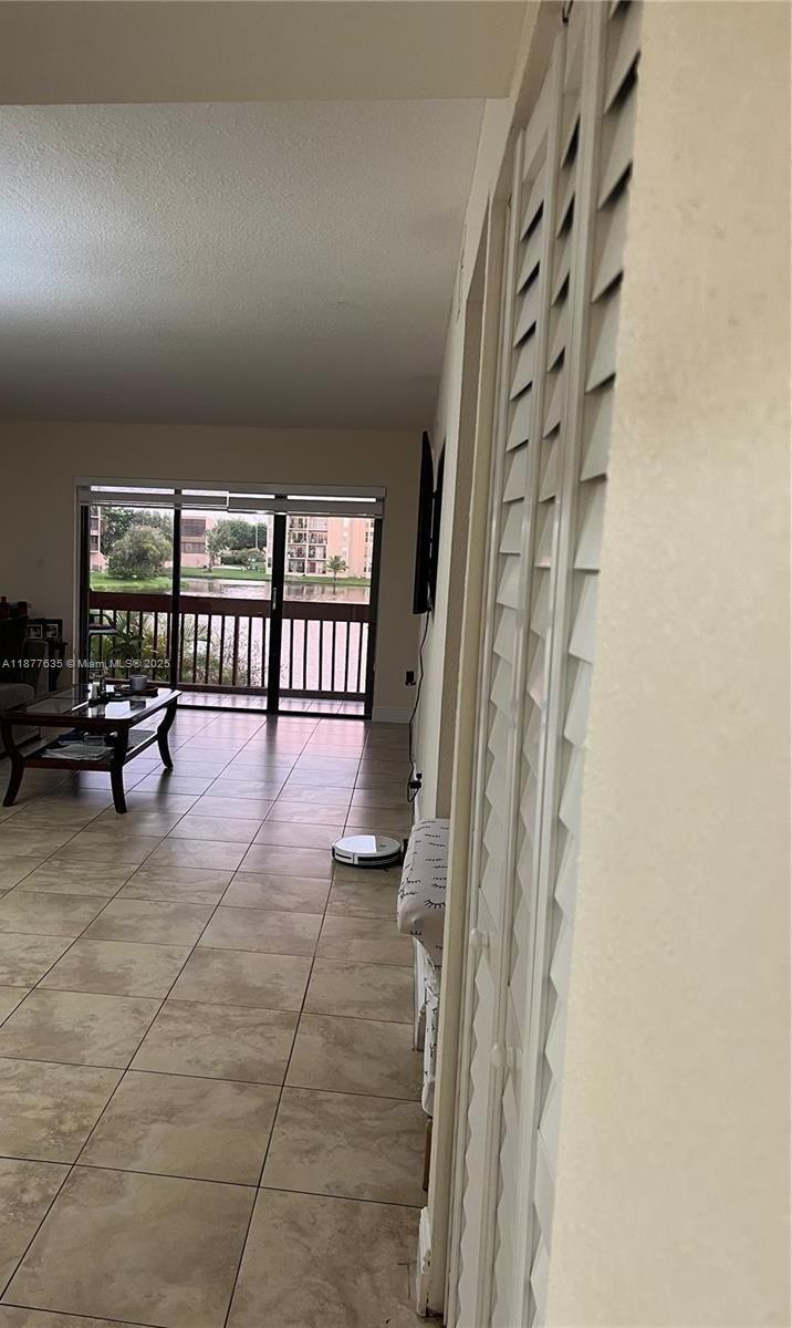 A living room with tile floors features a sliding glass door overlooking a lake — 8875 Fontainebleau Blvd # 203, Miami FL 33172, MIAMI, FL