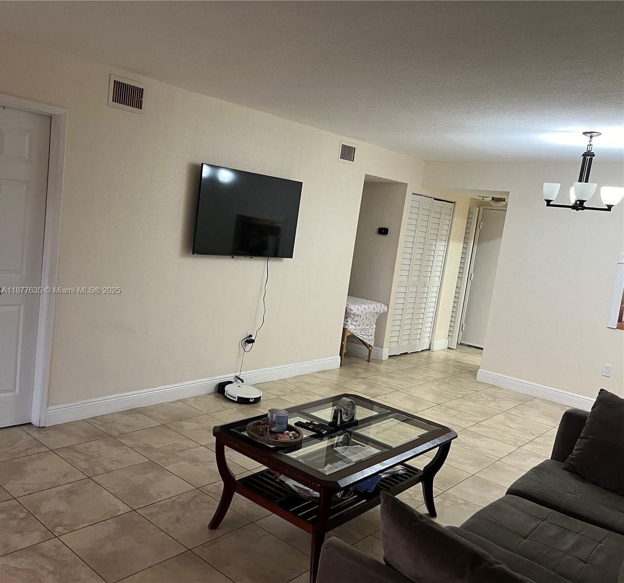 A living room features tile flooring, a wall-mounted television, and a glass-top coffee table — 8875 Fontainebleau Blvd # 203, Miami FL 33172, MIAMI, FL