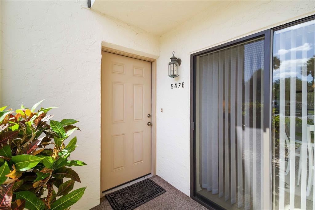 An exterior view shows a tan front door, a house number, and a sliding glass door — 5476 SWIFT ROAD UNIT 19, SARASOTA, FL