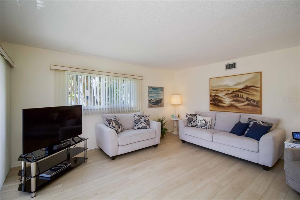 A living room features light wood flooring, a sofa, a loveseat, and a television stand — 5476 SWIFT ROAD UNIT 19, SARASOTA, FL