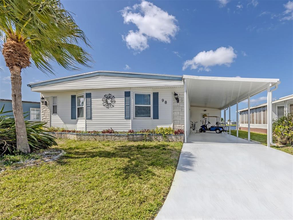 A single-story mobile home with white siding, blue shutters, and a covered carport — 98 LAKEVIEW DRIVE, NORTH PORT, FL