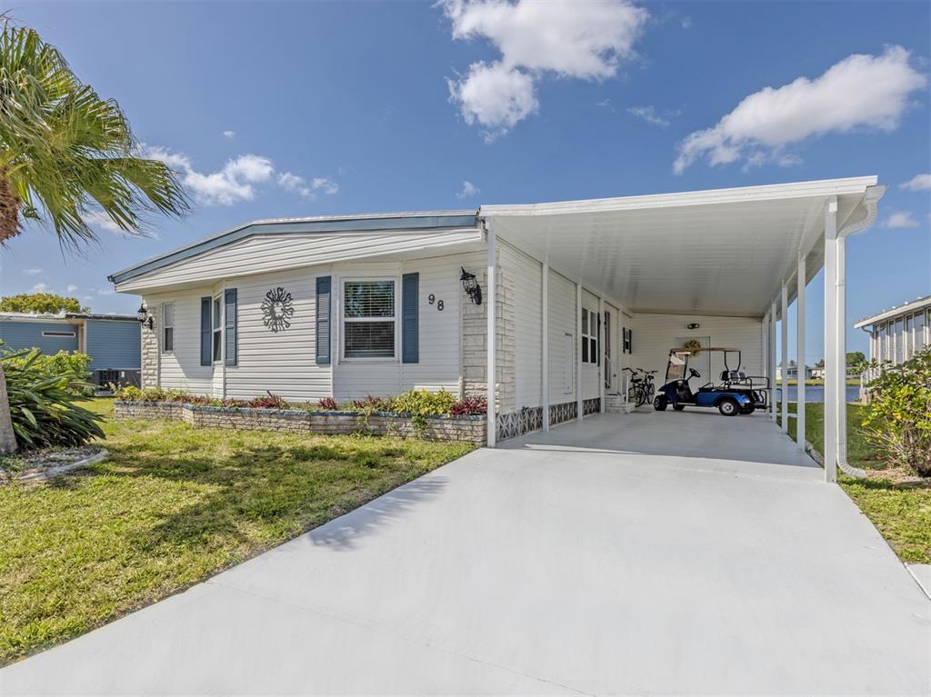 A white manufactured home with a carport, a golf cart, and a landscaped front yard — 98 LAKEVIEW DRIVE, NORTH PORT, FL